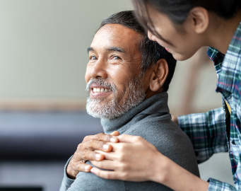 Smiling happy older Asian father with stylish short beard touching daughter's hand on shoulder looking and talking together with love and care.